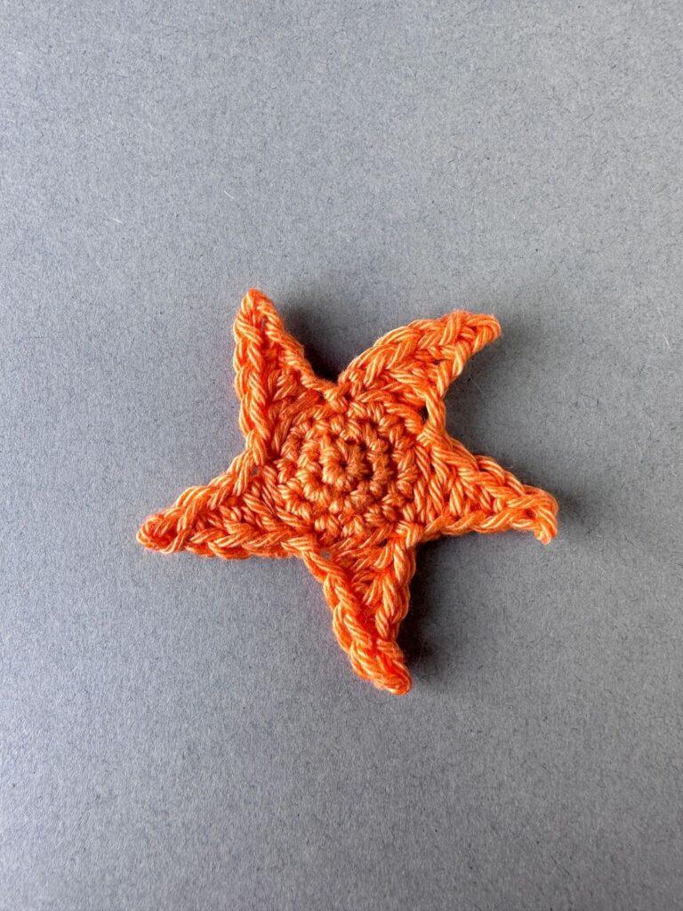 An orange crochet starfish appliqué on a grey background