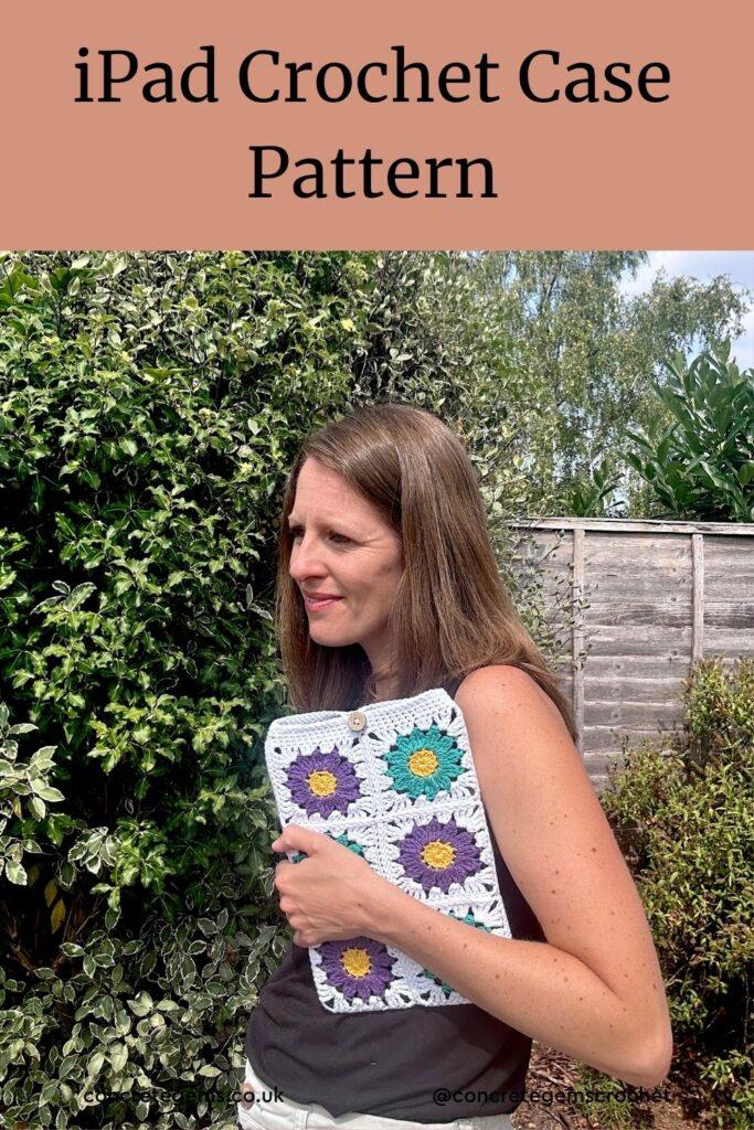 A lady holds a crochet iPad case under her arm in a garden. The crochet iPad cover features purple and teal floral granny squares