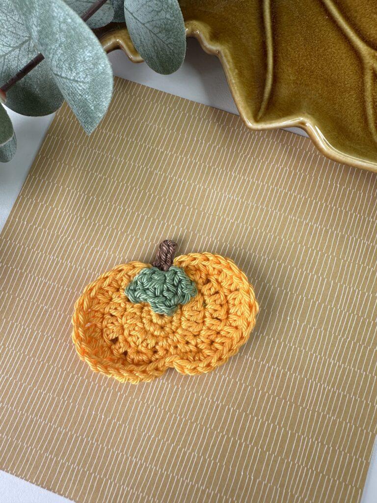 A single flat crochet pumpkin on a brown paper background