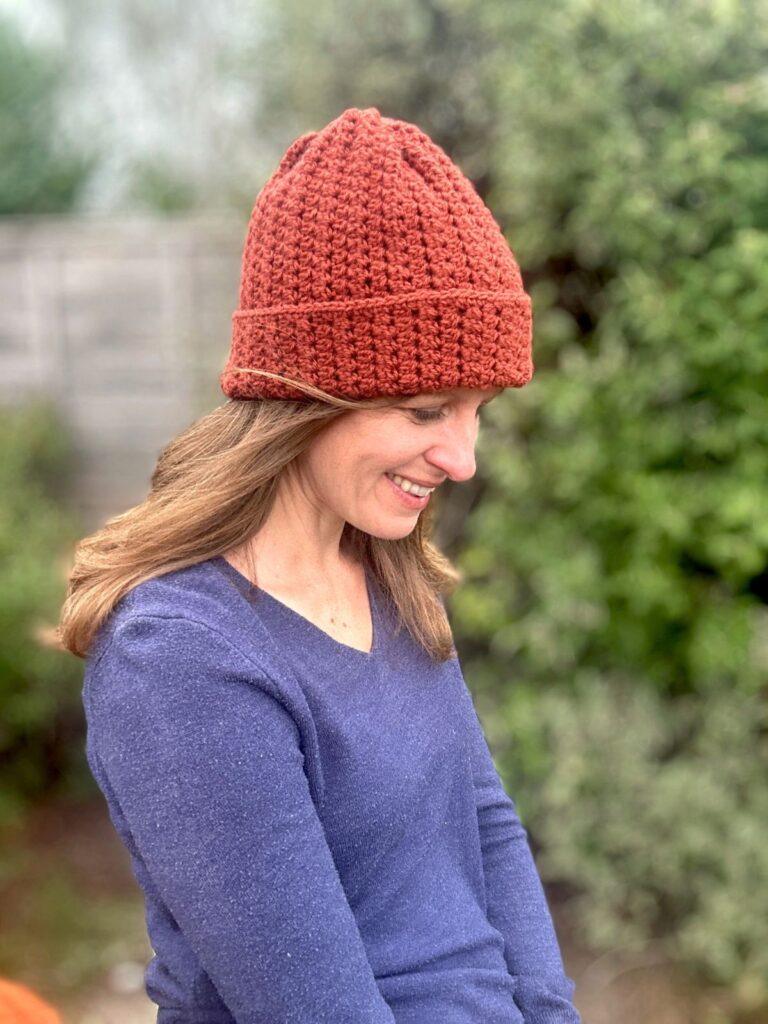 A lady smiling and looking down wears an orange textured crochet beanie