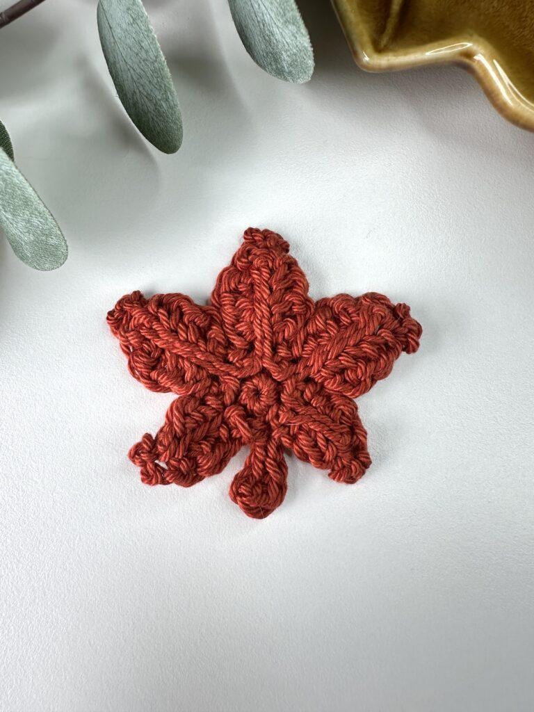 A red crochet maple leaf on a white background