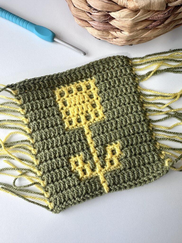 A mosaic crochet sunflower square in yellow with a green background