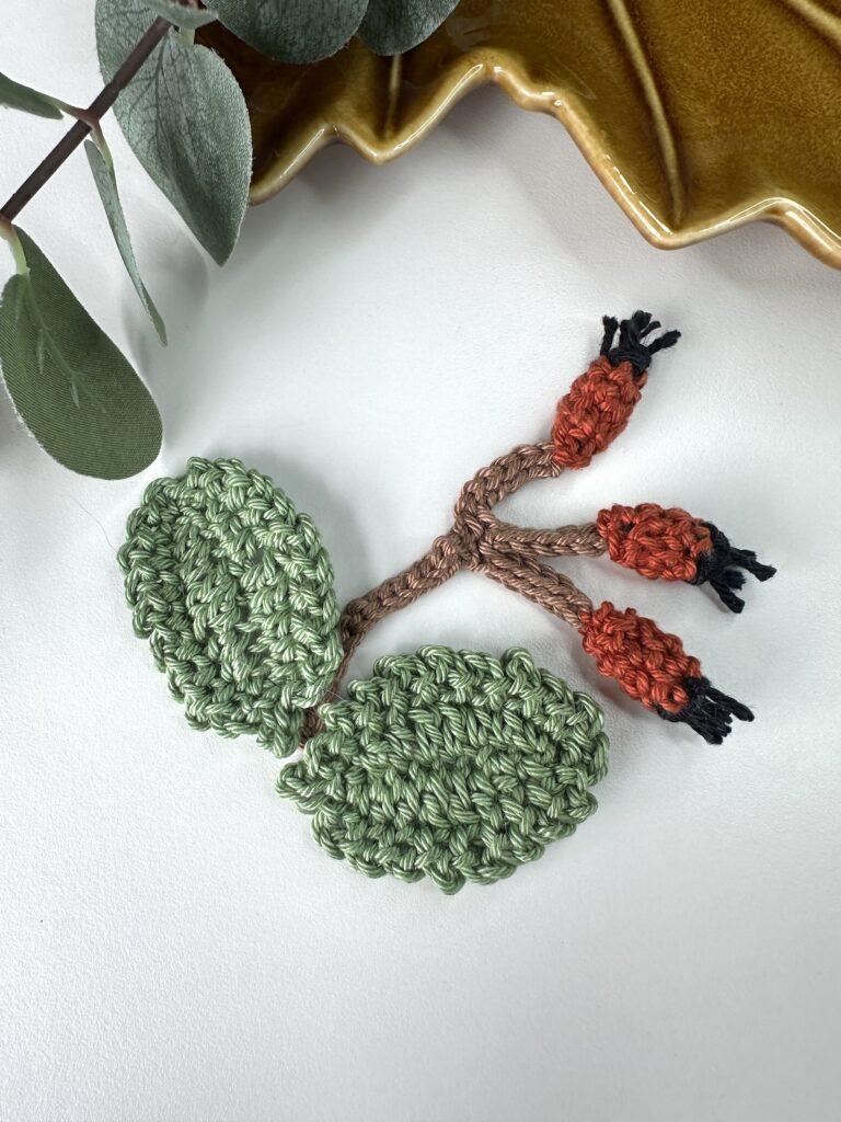 2 green crochet rose leaves and a crochet rose hip sprig