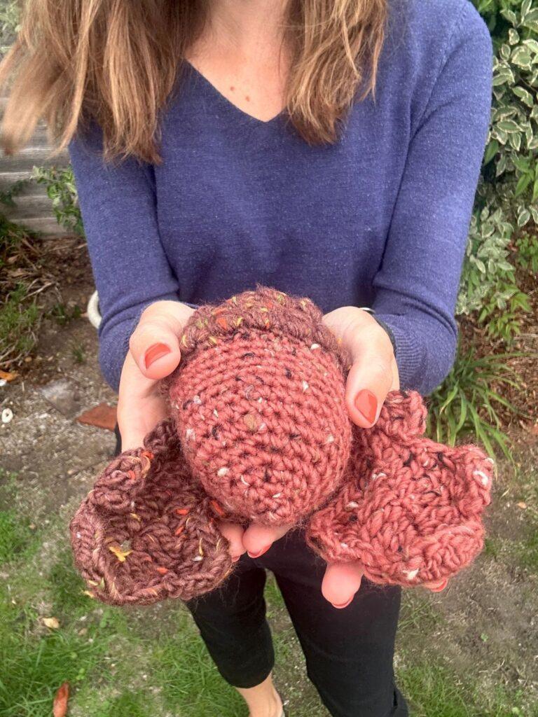 A lady holds a large crochet acorn and oak leaves in her hands