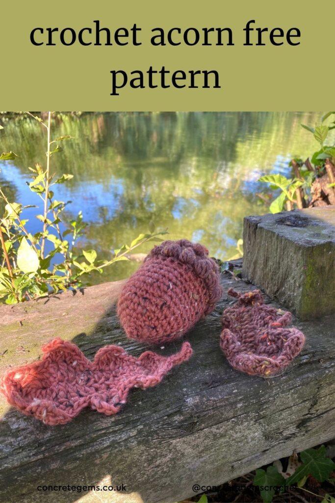 A crochet acorn in tweed yarn and crochet oak leaves are laid out by a lake