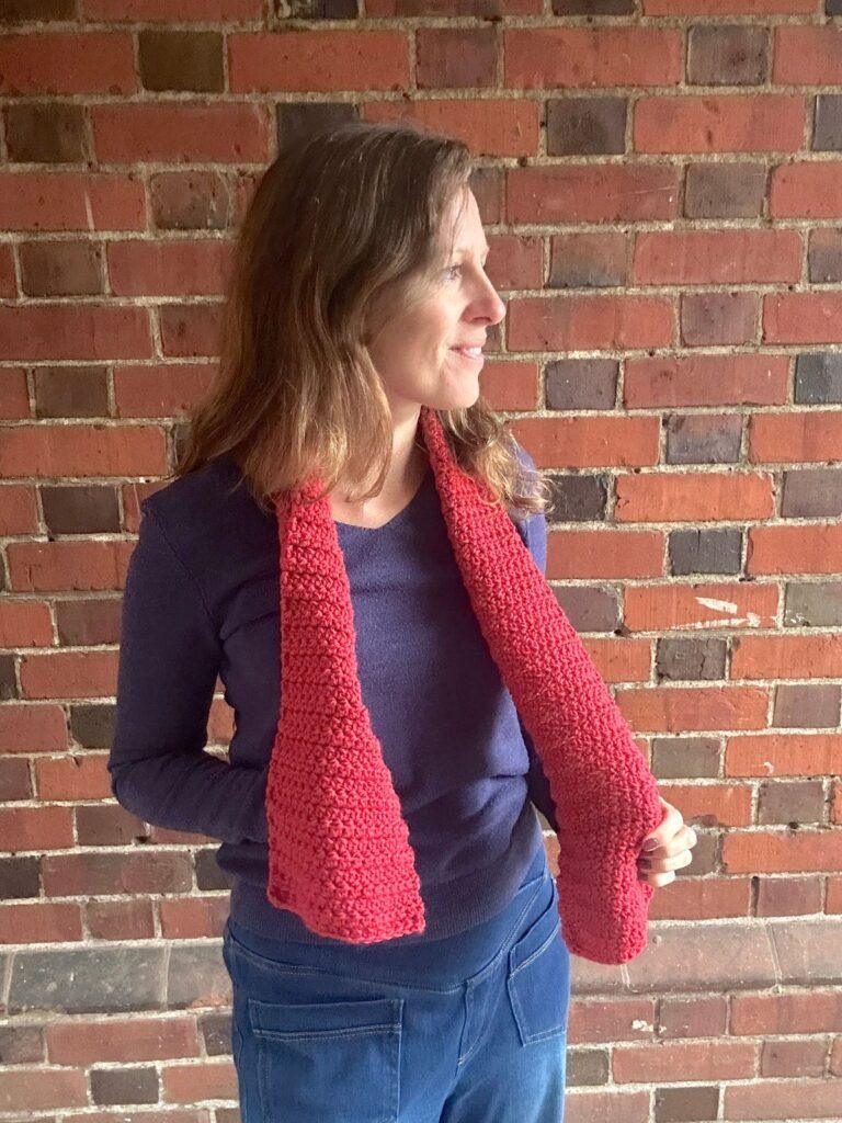 A woman has a thin red crochet scarf around her neck and looks off to the side
