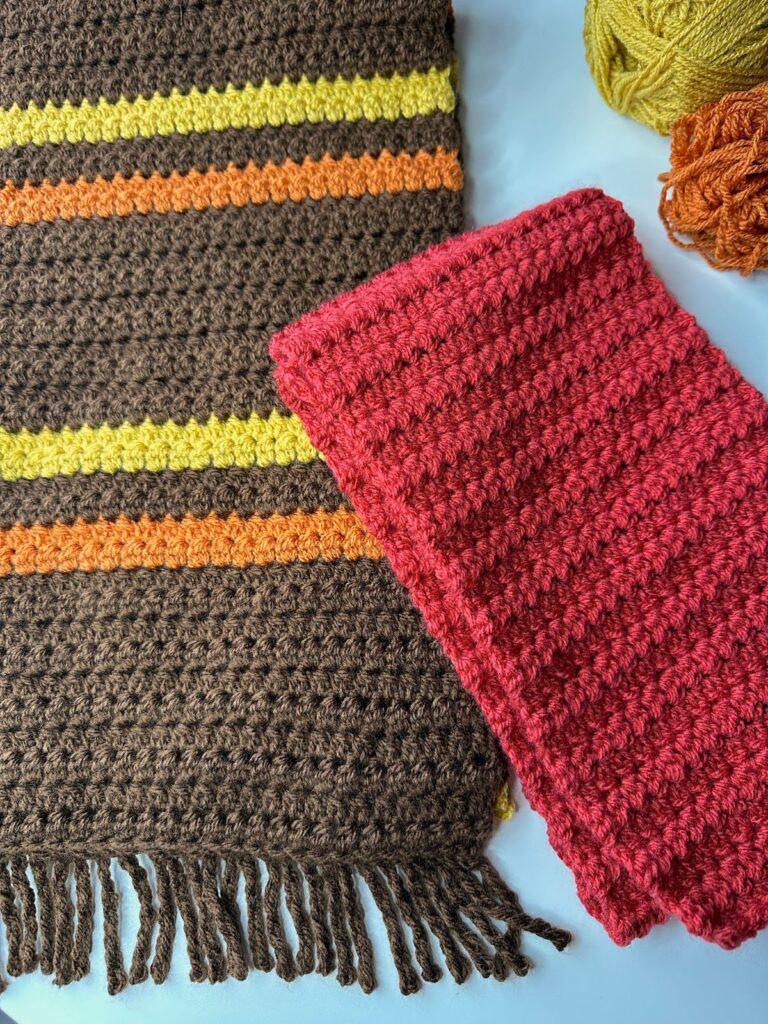 2 crochet scarves lay on a white surface, 1 is large and brown with orange and yellow stripes, the other is child size in red.