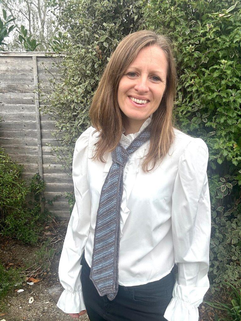 A woman wears a crochet mens tie in blue and grey with a white shirt