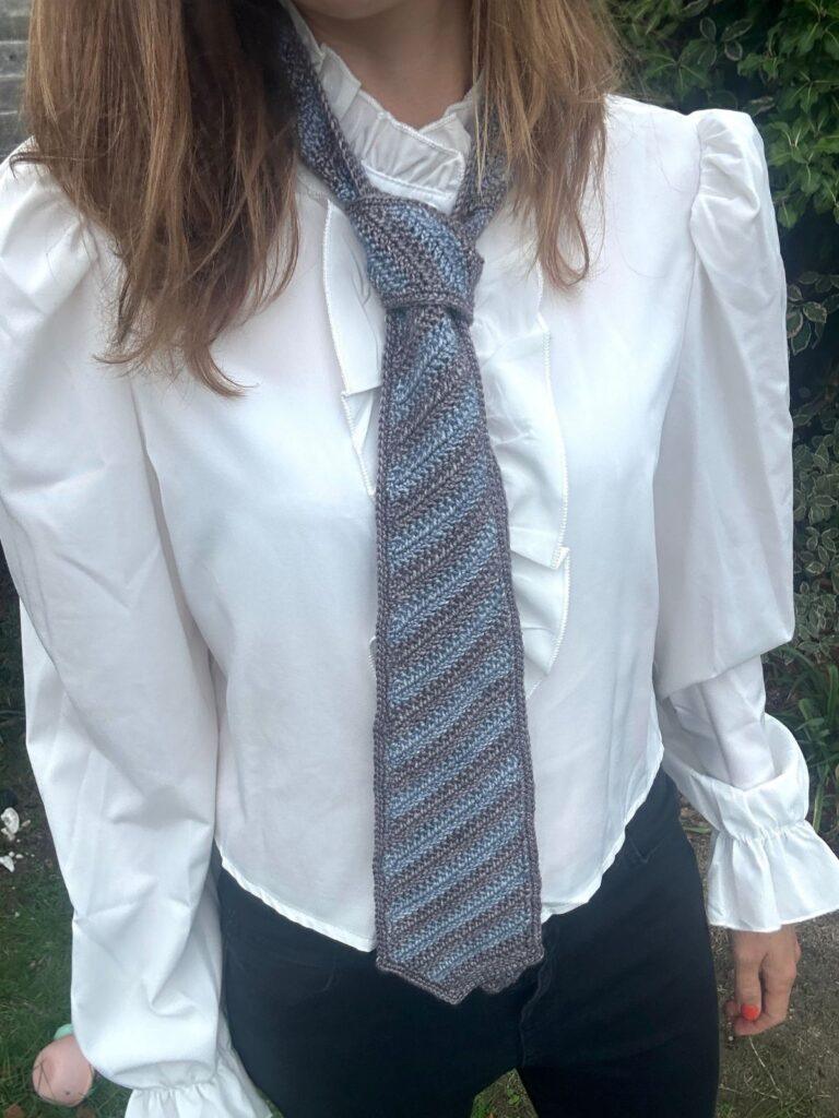 photo showing the torso of a woman wearing a white shirt and a blue and grey striped crochet men's tie